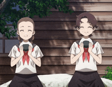 two girls in school uniforms sit on a rock with their hands folded in front of them
