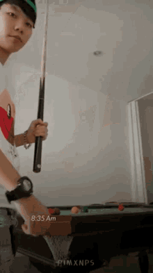a man holding a pool cue in front of a pool table with the time of 8:35 am