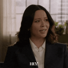 a woman in a suit says " hey " in front of a window