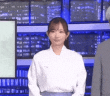 a woman in a white shirt is standing in front of a man in a suit in a newsroom .