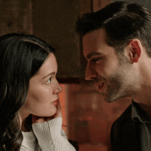 a man and woman are looking at each other and the woman is touching the man 's face