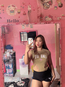 a girl taking a selfie in front of a mirror with hello kitty on the wall behind her