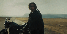 a man wearing sunglasses is standing next to a motorcycle on the side of the road .