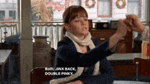 a woman sitting at a table with the words jinx back double pinky