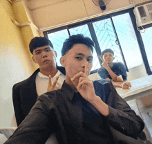 three young men are posing for a picture in a classroom with one man covering his mouth with his hand
