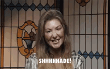 a woman is smiling in front of a stained glass window and saying shhhhhade