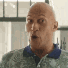 a bald man is making a surprised face while wearing a green and blue shirt .