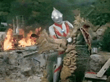 a man in a superhero costume is standing next to a monster in front of a building on fire .