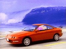 an orange car is parked on the side of the road in front of a large wave