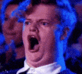 a man is making a funny face with his mouth open while sitting in a crowd .