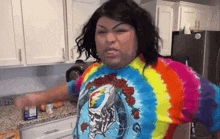 a woman in a kitchen wearing a tie dye shirt with a grateful dead skull on it