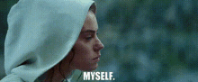 a woman wearing a white hooded sweatshirt is looking at the camera and says `` myself '' .
