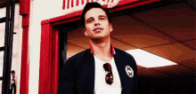 a man is standing in front of a red door wearing sunglasses and a jacket .