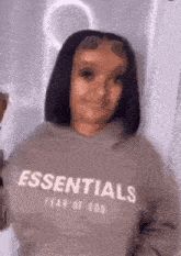 a woman wearing a sweatshirt that says `` essentials fear of god '' is making a funny face .