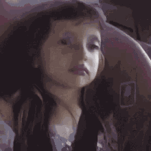 a little girl with purple lipstick on her lips is looking out of a window .