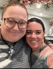 two women posing for a picture with one wearing glasses and a necklace