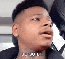 a young man is sitting in a car with his mouth open and says `` be quiet ! ''