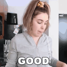 a woman with a ponytail is wearing a grey hoodie that says good on it