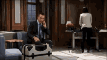 a man in a suit is talking on a cell phone while sitting on a suitcase .