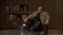 a man in a suit sits in a chair with his feet on a glass table with maybe baby written above him