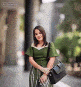 a woman in a green top and green striped pants is holding a black briefcase and smiling