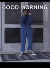 a man in a blue jumpsuit is standing in front of a door with the words `` good morning '' written above him .