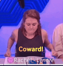a woman in a black tank top is sitting at a table with the words coward written on it .