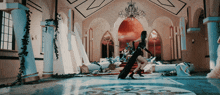 a woman in a black dress is standing in a room with a chandelier