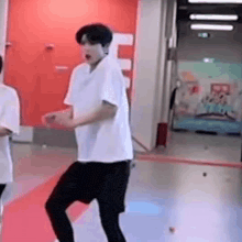 a man in a white shirt and black shorts is dancing on a red carpet in a gym .