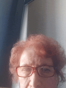a woman with red hair wearing glasses looks at the camera with her eyes closed