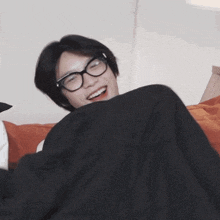 a young man wearing glasses is laying on a bed with a black blanket