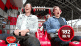 two women are riding a roller coaster with a 182 km / h sign in front of them
