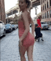 a woman in a short pink dress is standing on a brick sidewalk .