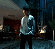 a man in a grey sweater stands in a dark room with his hands in his pockets