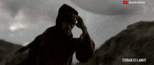 a man in a hooded jacket is standing in front of a mountain with the words terbaik ke langit written below him