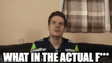 a man sitting on a couch with the words " what in the actual f *** " written on the screen