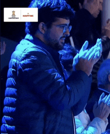 a man in a blue jacket is clapping his hands in a crowd