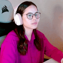 a woman wearing glasses and headphones sits in front of a corsair chair