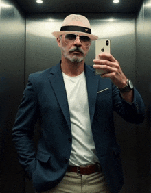 a man wearing a hat and sunglasses takes a selfie with his iphone