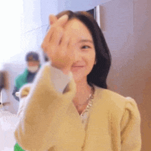 a woman in a yellow sweater is making a heart with her hands .
