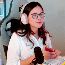 a woman wearing headphones and glasses is sitting in front of a microphone holding a cell phone