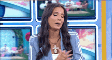 a woman wearing a blue jacket and a cross necklace is standing in front of a television .