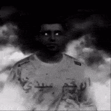 a black and white photo of a man wearing a white shirt with arabic writing on it