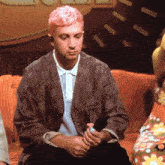 a man with pink hair sits on an orange couch