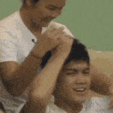 a woman is brushing a man 's hair while a man looks on .