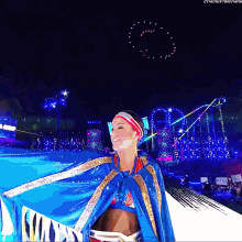 a woman in a blue cape is standing in front of a stage with a sign that says the next thing