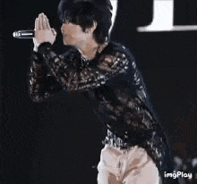 a man is singing into a microphone while wearing a black lace shirt .