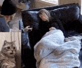 a man is petting a cat while a woman is sleeping on a couch covered in a blanket .