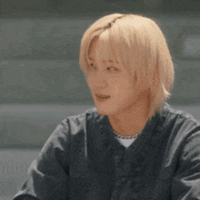 a young man with blonde hair is wearing a grey shirt and a white shirt .