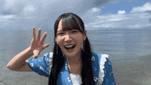 a woman in a blue shirt is waving her hand in front of the ocean